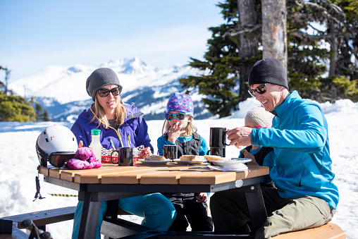 Ski family enjoy snack outdoors at Canadian ski resort on a sunny winter day