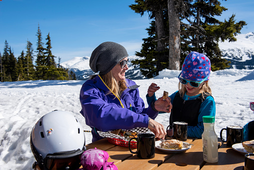 Ski family enjoy snack outdoors at Canadian ski resort on a sunny winter day