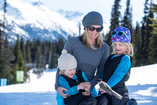 Mother and daughters hold wild bird on ski slope at Canadian ski resort on a sunny winter day