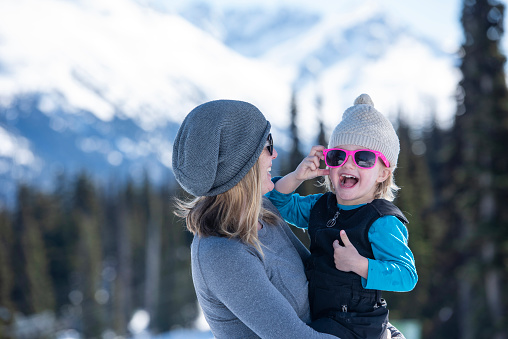 Mother and daughter pause on ski slope at Canadian ski resort on a sunny winter day