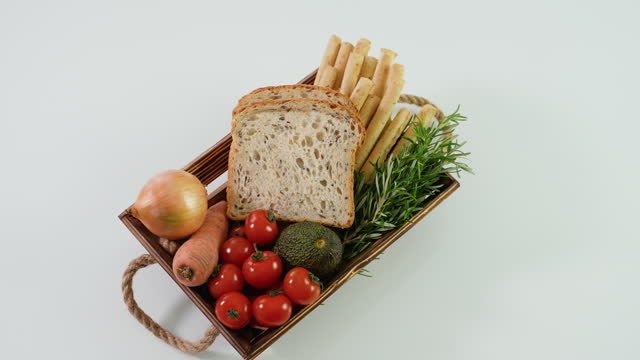 Wooden basket with fresh vegetables, cheese bread sticks and fresh toaster bread on white