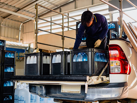 Workers lift drinking water bottles in crates into the back of a transport truck purified drinking water inside the production line to prepare for sale. Water drink factory, small business