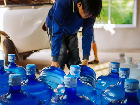 Workers lift drinking water 
clear and clean in blue plastic gallon into the back of a transport truck purified drinking water inside the production line to prepare for sale. Water drink factory, small business
