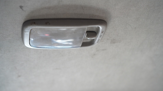 The top light from the interior of a very old gray car is still usable