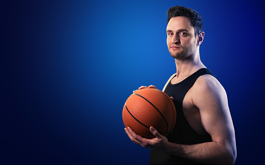 Young white professional basketball player holding a ball in his hands, standing in a heroic pose