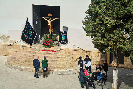 Tarragona, Spain - April 16, 2024: A golden sculpture of Christ crucified adorns a church during Holy Week, surrounded by faithful from the gypsy community and floral decorations capturing a moment of devotion and brotherhood.