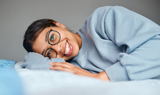 Woman, portrait and relax in bed with glasses in morning, resting and happy for weekend or vacation in London. Female person, girl and smile in bedroom at apartment with duvet and comfortable for nap