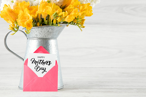 Beautiful yellow and white flowers in a vase with mother’s day message on wooden background