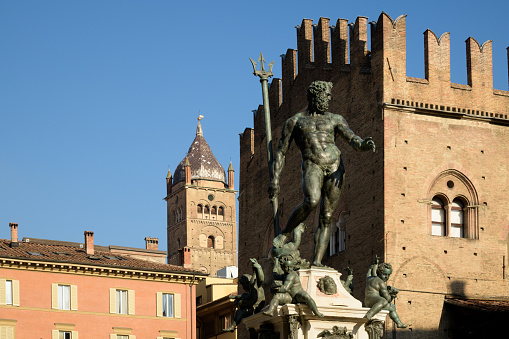 Neptune Fountain commands attention in Bologna, its statue set against historic buildings and a vivid blue sky, capturing the essence of Italian grandeur