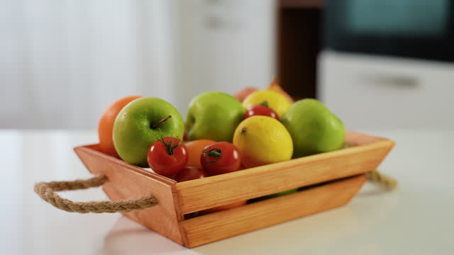 Wooden basket with fresh fruits and vegetables on table in kitchen. Vegetarian breakfast