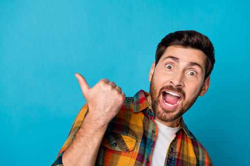 Portrait of astonished guy with stubble wear plaid shirt scream directing at black friday empty space isolated on blue color background.
