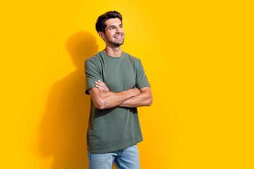 Photo of dreamy confident man with bristle dressed khaki t-shirt arms folded look at offer empty space isolated on yellow color background.