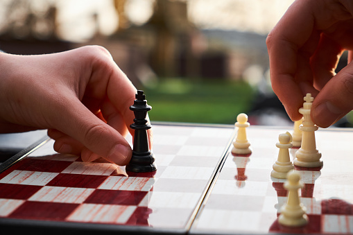 The chess board is made of wood. Person playing chess in nature. The person is holding a black king in their hand.