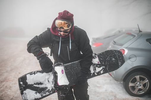A male snowboarder prepares for the adventure of going down the mountain on a snowboard during a winter day