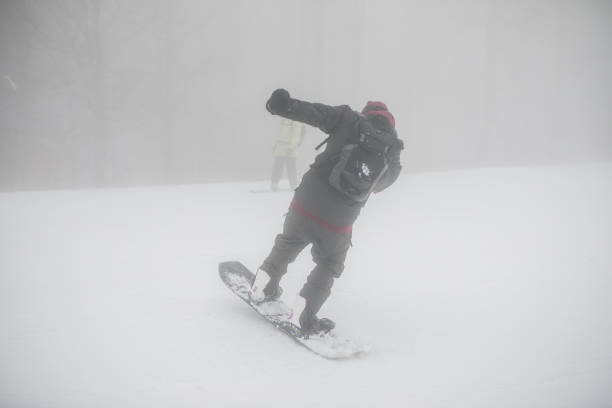 A snowboarder with gear is snowboarding on a mountain during a foggy day. He performs acrobatics and enjoys the adrenaline that this extreme winter sport provides