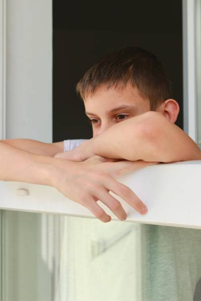 a young boy is leaning on a window sill and looking out.