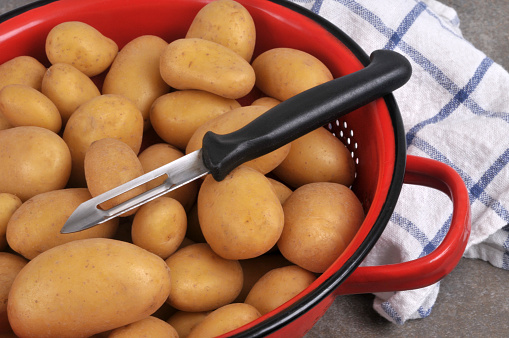Raw unpeeled potatoes in a red colander with a peeler close-up