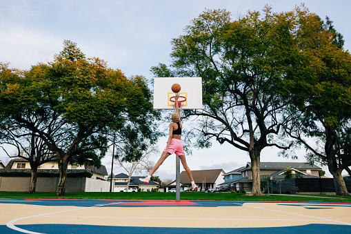 Woman playing at outdoor basketball court in a public park.