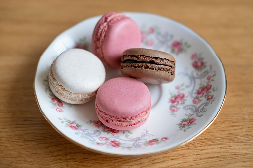 Four delicate macaroons placed on a porcelain plate, confectionery popular for the light texture, selection of fruity flavors and guilty-free petite size, elegant dessert for parties or gatherings.