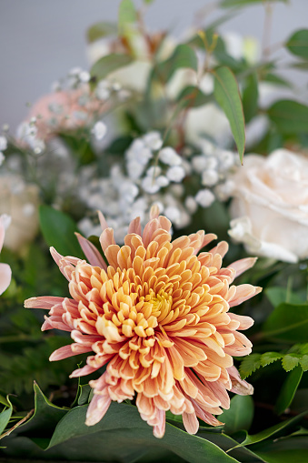 Details of a large bridal table floral centerpiece with focus on a large orange chrysanthemum, elegant flower arrangement brightening up the space: a restaurant or a reception area for the wedding day.