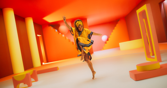 Beautiful Black Woman in African Outfit Dancing Energetically in Geometric Abstract Orange Environment. Creative Female Performing Dance Choreography in a Studio While Looking at the Camera.
