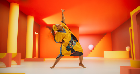 Beautiful Black Woman in African Outfit Dancing Energetically in Geometric Abstract Orange Environment. Creative Female Performing Dance Choreography in a Studio, Making Moves, Having Fun, Practicing