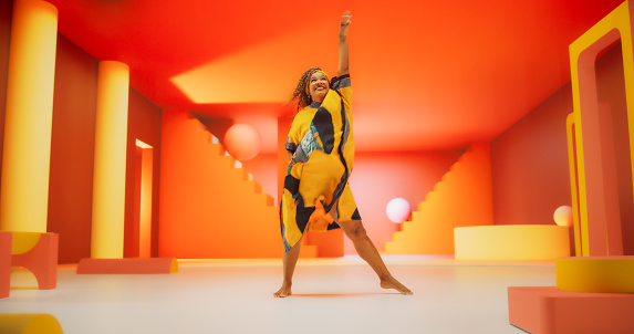 Beautiful Black Woman in African Outfit Dancing Energetically in Geometric Abstract Orange Environment. Creative Female Performing Dance Choreography in Bright Studio, Making Moves, Having Fun.
