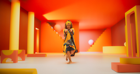 Beautiful Black Woman in African Outfit Dancing Energetically in Geometric Abstract Orange Environment. Creative Female Performing Dance Choreography in a Studio, Making Moves, Having Fun.