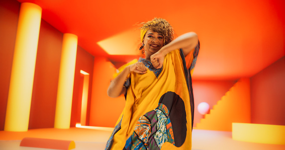 Beautiful Black Woman in African Outfit Dancing Energetically in Geometric Abstract Orange Environment. Creative Female Performing Dance Choreography in Bright Studio, Making Moves, Practicing.