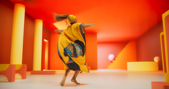 Beautiful Black Woman in African Outfit Dancing Energetically in Geometric Abstract Orange Environment. Creative Female Performing Dance Choreography in Studio, Making Moves, Having Fun, Practicing