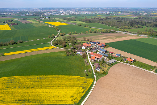 Aerial view of a landscape with a village among green and yellow canola fields in spring.