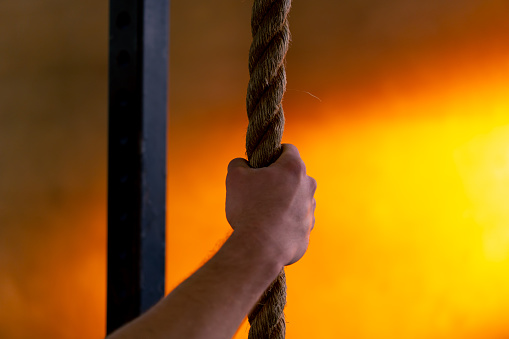 close-up in a sports club of a hand holding ropes for exercise on a bright orange background