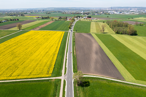 Aerial view of a spring, rural landscape with a road among green and yellow canola fields.