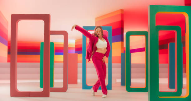 istock Stylish Professional Female Dancer Performing a Modern Dance Routine in Front of Big Led Wall Screen with Colorful Striped Background During a Virtual Production in Studio Environment 2148828903