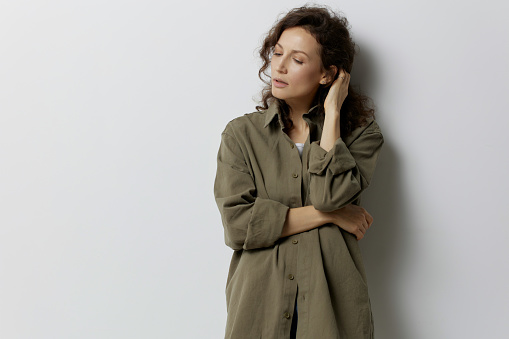 Frustrated pensive curly beautiful woman in casual khaki green shirt thinks about abusive relationships looks aside posing isolated on white background. People Emotions Lifestyle concept. Copy space