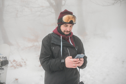 Winter sport and recreation, leisure outdoor activities. Man in ski equipment with smartphone. Snowboarder man hiking at mountain