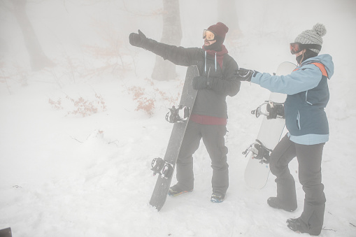 Two snowboarders stand in the middle of a mountain and think about where to go down with their snowboard
