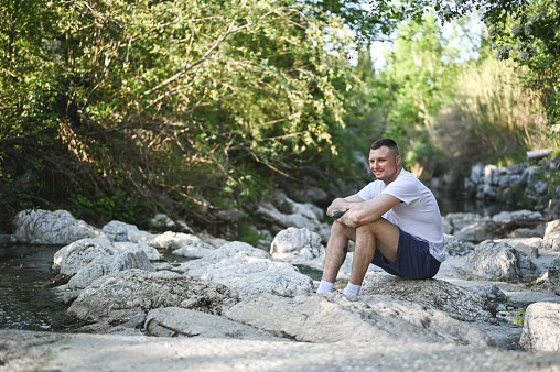 Young man sitting on a stone near river.
