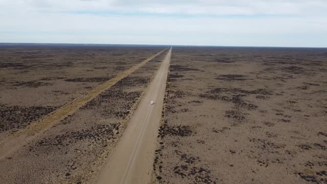 Aerial video high view of a small white van driving on a straight gravel road on flat arid landscape
