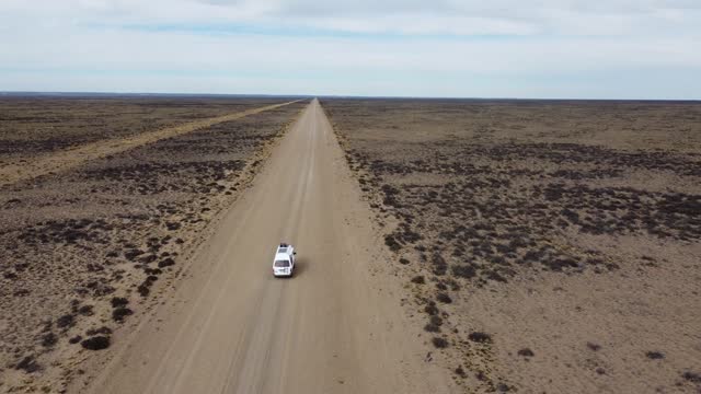 Aerial video following a small white van driving on gravel road on flat arid landscape