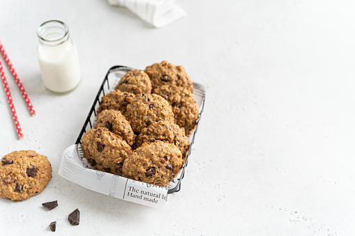 Healthy oat cookies in a basket and bottle of milk on white background. Homemade flour free oatmeal cookies with banana, oats, nuts, eggs, chocolate drops. Gluten free oatmeal biscuits. Copy space
