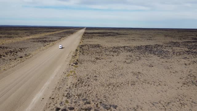 Aerial video rear view of small white van driving on gravel road on flat arid landscape