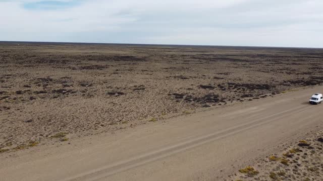 Aerial video front view of small white van driving on gravel road on flat arid landscape