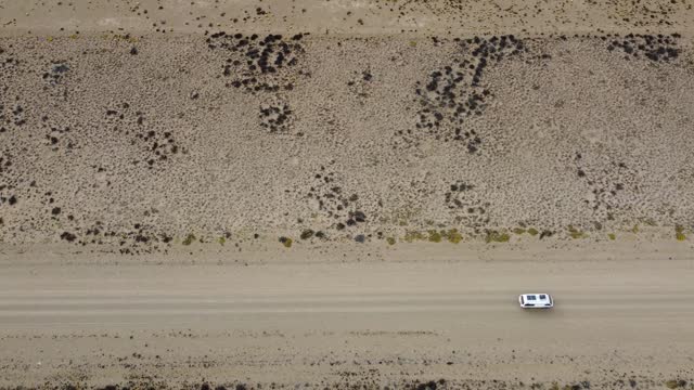 Aerial video top down view of a small white van driving on a straight gravel road on flat arid landscape