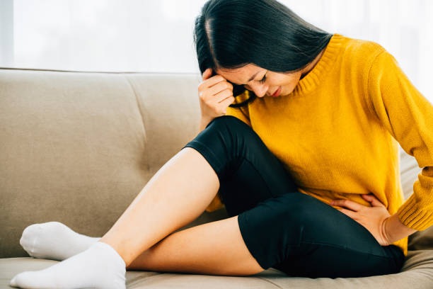 istock Asian woman seated on a home couch experiences abdominal pain 2148837101