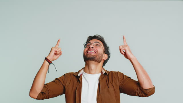 Young man showing thumbs up and pointing overhead on blank space place for your advertisement logo