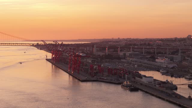 Panoramic aerial overview of port cranes on Tagus river in Lisbon Portugal, establishing at sunset