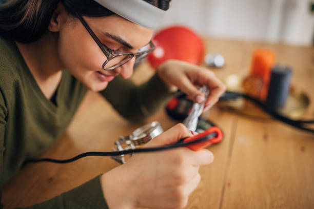 Focused young Caucasian woman with soldering iron fixing a megaphone in a cozy home setting.
