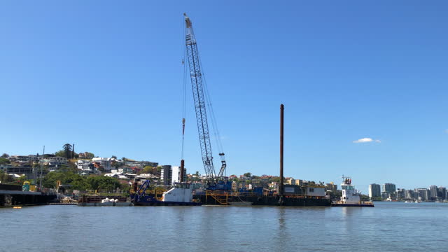 A construction crane sitting on a barge being towed by two tug boats ready to build a bridge across a river