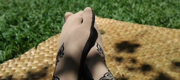View of woman wearing socks, sitting on a purun mat in park (garden), on the green grass